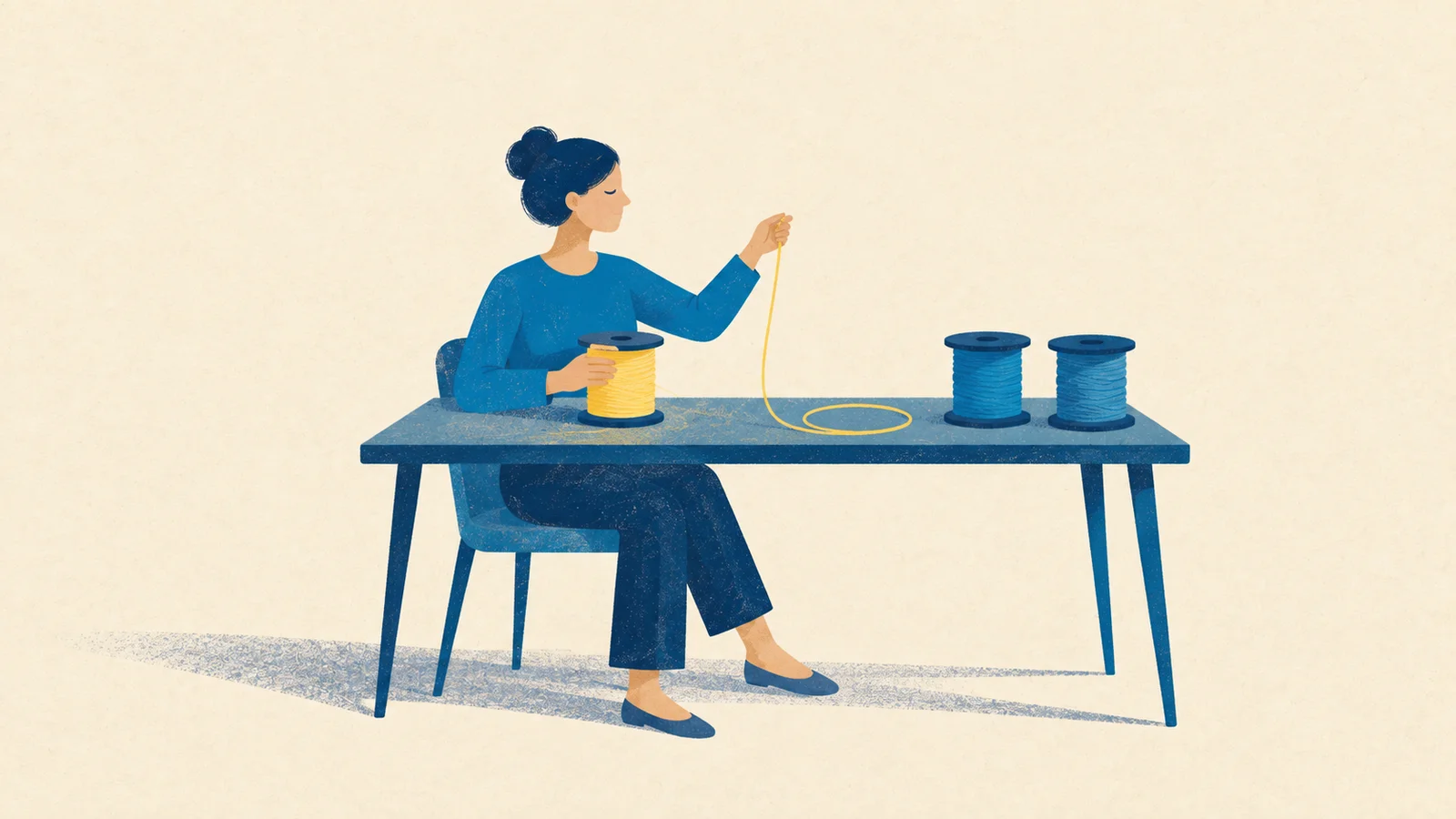 Mulher trabalha com um fio amarelo enquanto dois outros carretéis azuis aguardam sobre a mesa.